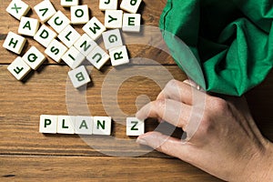 Hand placing the letter Z next to the word PLAN on a wooden background