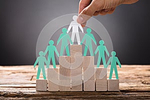 Hand Placing Paper Businessman With Employees On Pyramid Blocks