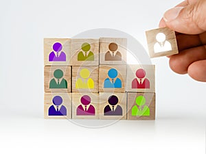 A hand placing a wooden block with colorful people icon onto many others, putting the right man into the right position, HR