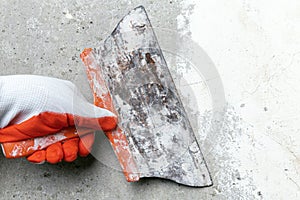 Hand of plasterer holds old trowel, scrubbing concrete wall, removes old plaster during redecoration