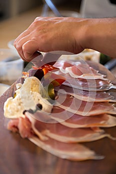 Hand plating appetizers on a wooden board with proscuitto.