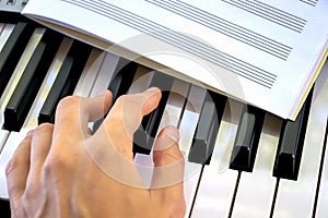 Hand play black and white piano keys a notebook for sheet music lies learning music sheet music playing on the synthesizer