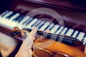 Hand playing the violin with blurry piano in music room or stage