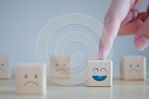 Hand point to happy face among unhappy faces on wooden blocks. Positive thinking and World mental health day concept.