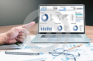 Hand pointing finger to mock up sales summary slide show presentation on display laptop with pen ,glasses and paper work on table