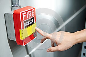 Hand pointing at fire alarm switch on the wall