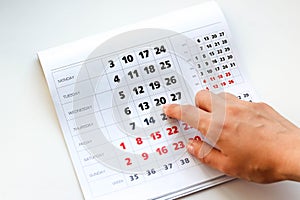 Hand pointing to the calendar. White calendar. Weekends are highlighted in red. Close up