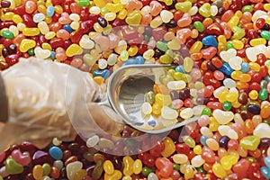 Hand in polyethylene glove holding metallic scoop with colorful candys sweets in confectionery store. Selective fokus