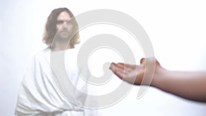 Hand of poor man praying to God, asking for wealth, Jesus standing in light