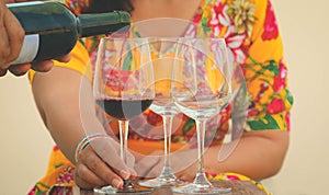 Hand poring red wine to wine glasses on table,