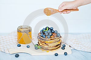 Hand pour honey on pancakes with blueberries