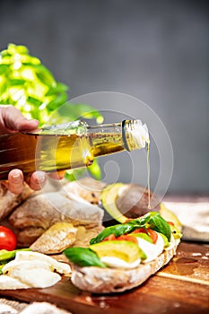 Hand is pouring basil`s olive oil on the sandwich