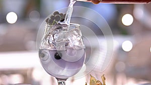 Hand pouring drink into glass with ice cubes.