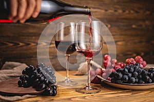 Hand is pouring dry red wine from a bottle into a glass on a wooden table. Concept of viticulture and winemaking