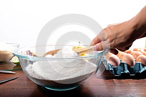 Hand pouring flour into a bowl with a wooden spoon. Using wooden spoon to pour wheat flour into transparent container.