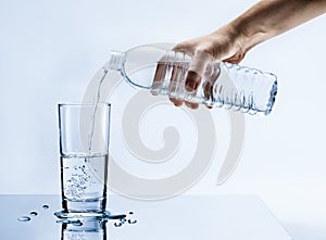 Hand pouring fresh pure water from bottle into a glass on the table with water drops