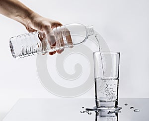 Hand pouring fresh pure water from bottle into a glass on the table with water drops