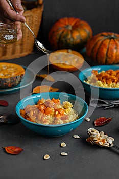 Hand pouring honey over bowl of millet porridge with pumpkin