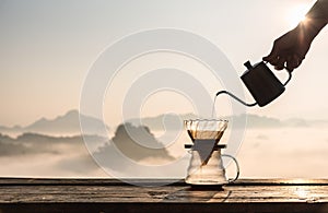 Hand pouring hot water on coffee ground with fillter, barista using drip coffee kit set with mountain and fog in sunrise