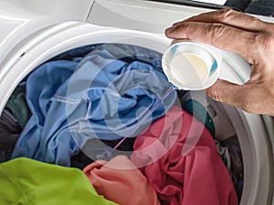 Hand pouring laundry detergent with colorful clothes in washing machine