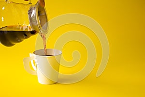 Hand pouring liquid coffee put in the cup on a yellow paper background. Copy space for your text