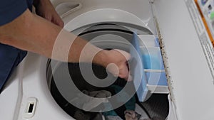 Hand pouring liquid detergent into washing machine.