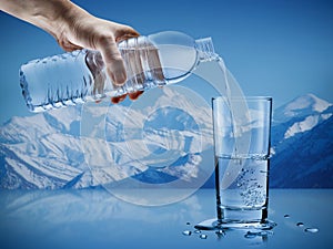 Hand pouring mineral water from bottle into a glass with water drops in the iceberg background