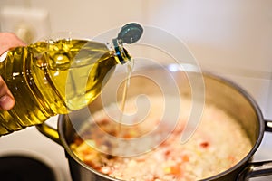 Hand pouring olive oil into a cooking pot