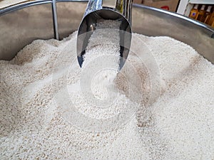 Hand pouring raw uncooked heap of rice with measuring mug dispensing container at supermarket for sale