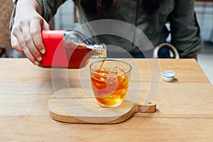 Hand pouring red label Cold Brew Tea in drinking glass with ice on wooden table