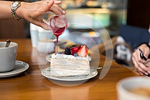 Hand pouring strawberry sauce over crape cake