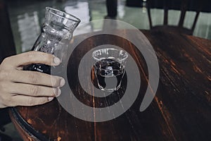 Hand pouring of v60 black coffee from unique beaker coffee glass jar on the wooden table