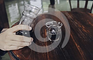 Hand pouring of v60 black coffee from unique beaker coffee glass jar on the wooden table