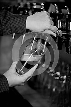 Hand pours a beer in a transparent glass from the tap.Retro b W