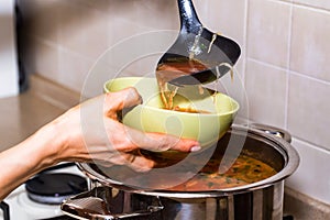 Hand pours borscht or red vegetable soup in bowl