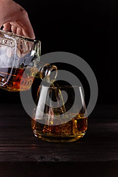 A hand pours brandy from a decanter into a glass. Alcoholic beverages, dark background. Vertical orientation