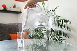 A hand pours purified filtered water into a glass