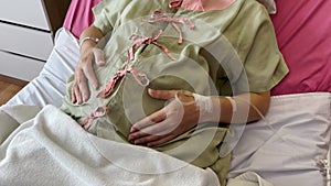 Hand of pregnant woman stroking her belly on a bed in hospital