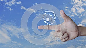 Hand pressing house with shield icon on finger over blue sky with white clouds, Business home insurance and security concept