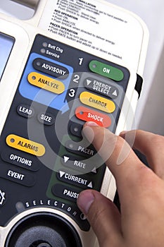 Hand pressing a red shock button on a modern defibrillator