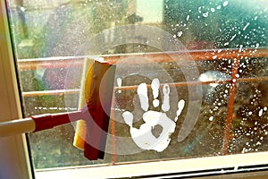 Hand print on dirty window and squeegee cleaning the glass.