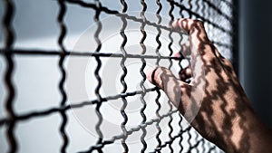 Hand of prisoner holding rustic metal fence with pattern shadow, criminal locked in jail