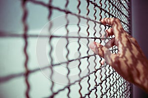 Hand of prisoner holding rustic metal fence with pattern shadow, criminal locked in jail, dream of freedom concept