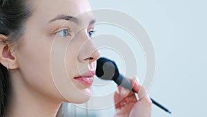 Hand of professional make-up artist covering powder using fluffy brush face of young fashion model