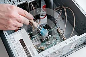 Hand of professional repairman holding a cleaning brush inside old personal computer