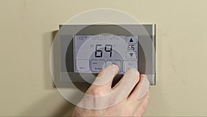 Hand programming digital thermostat on wall