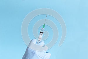 Hand in protective blue gloves hold medicine syringe with vaccine on blue background. Concept of vaccination and healthcare