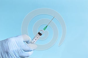 Hand in protective blue gloves hold medicine syringe with vaccine on blue background. Concept of vaccination and healthcare