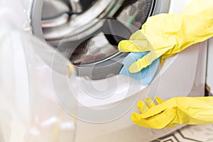 Hand in protective glove carefully cleaning the washing machine. Regular clean up. Maid cleans house