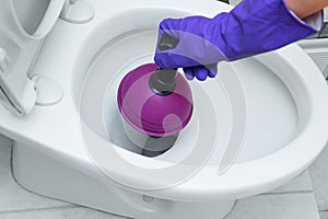 A hand in a protective glove cleans blockage in the toilet bowl with a plunger